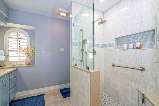 bathroom featuring wood finished floors, walk in shower, vanity, and baseboards