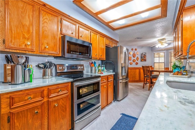 kitchen featuring wainscoting, brown cabinets, stainless steel appliances, a textured ceiling, and a sink