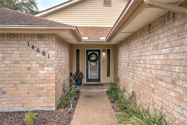 property entrance with an attached garage, a shingled roof, and brick siding