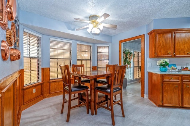 dining space with wooden walls, wainscoting, ceiling fan, light wood-style flooring, and a textured ceiling