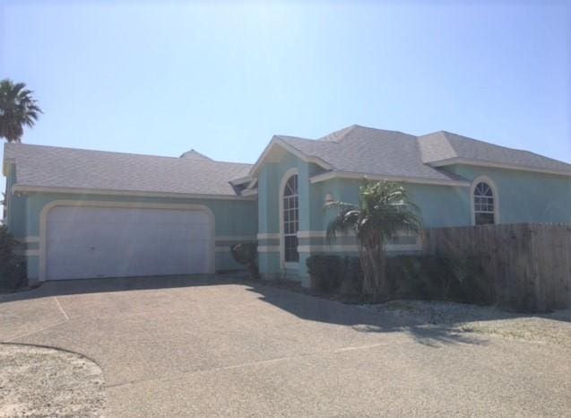 view of front of home with driveway, an attached garage, fence, and stucco siding