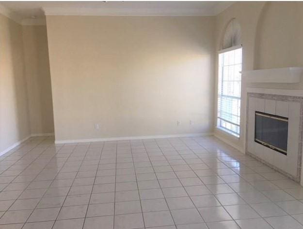 unfurnished living room featuring baseboards, a fireplace, light tile patterned flooring, and crown molding