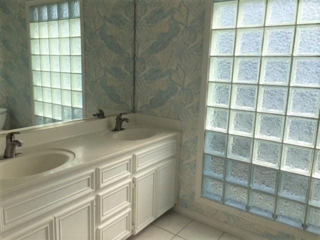 bathroom featuring double vanity, tile patterned floors, a sink, and wallpapered walls