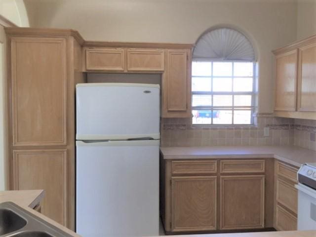 kitchen with light countertops, white appliances, light brown cabinets, and decorative backsplash