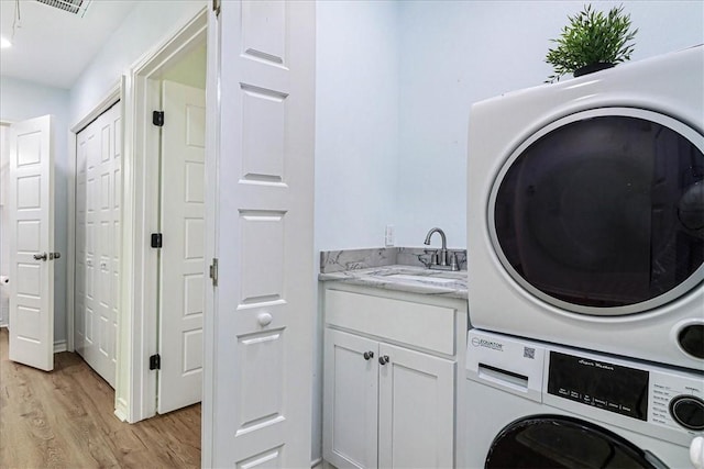 clothes washing area featuring a sink, light wood-style floors, and stacked washing maching and dryer