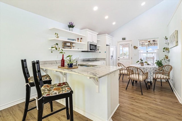 kitchen with light stone counters, open shelves, light wood-style floors, white fridge with ice dispenser, and stainless steel microwave