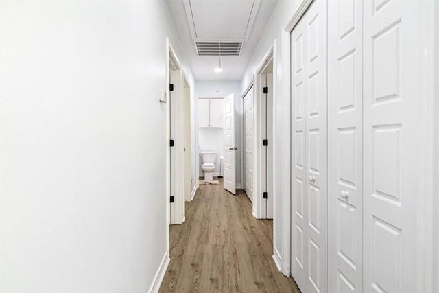 hall with visible vents, baseboards, attic access, and wood finished floors