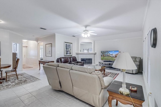 living room featuring crown molding, ceiling fan, a tiled fireplace, and light tile patterned floors