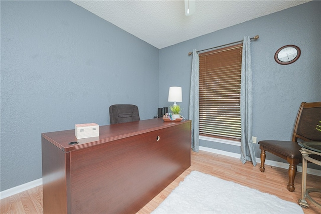 home office with a textured ceiling and light hardwood / wood-style flooring