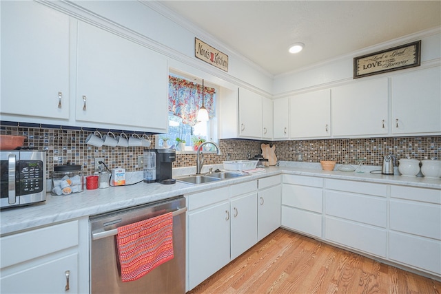 kitchen with stainless steel appliances, white cabinetry, sink, ornamental molding, and light hardwood / wood-style flooring