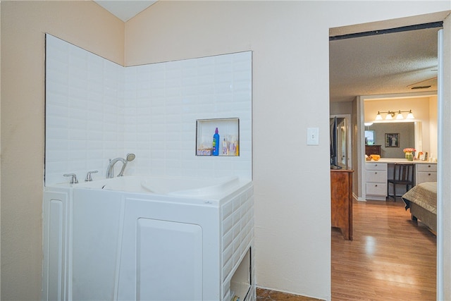 bathroom with hardwood / wood-style floors, a textured ceiling, a bath, and vanity