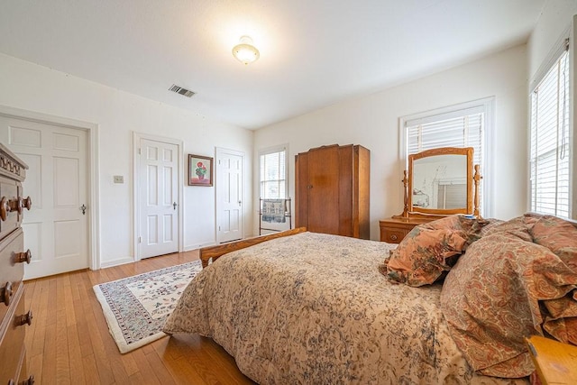 bedroom with multiple closets, multiple windows, visible vents, and light wood finished floors