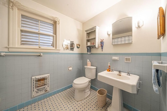 bathroom with toilet, a wainscoted wall, heating unit, tile patterned flooring, and tile walls