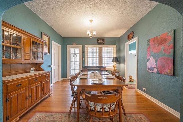 dining room featuring light wood finished floors, baseboards, an inviting chandelier, and a textured wall