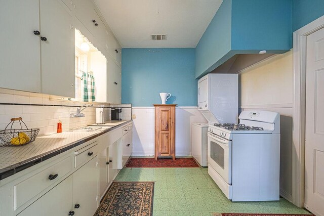 kitchen with white range with gas stovetop, a sink, visible vents, wainscoting, and light floors