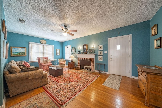 living room featuring a ceiling fan, a brick fireplace, visible vents, and wood finished floors