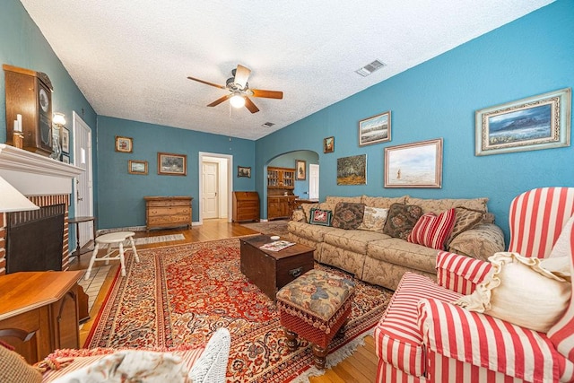 living area featuring arched walkways, a fireplace, visible vents, ceiling fan, and wood finished floors