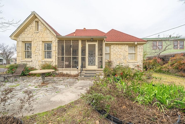 back of house featuring a sunroom, a patio area, and stone siding