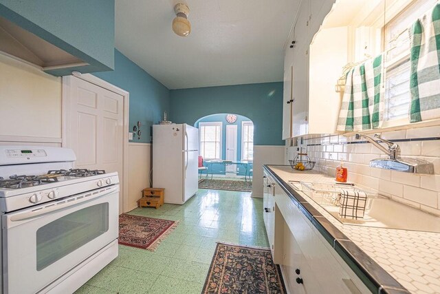 kitchen featuring arched walkways, white appliances, light countertops, and white cabinetry