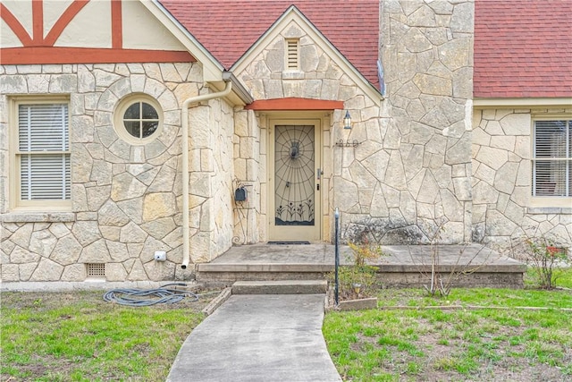view of exterior entry featuring crawl space, stone siding, a yard, and roof with shingles