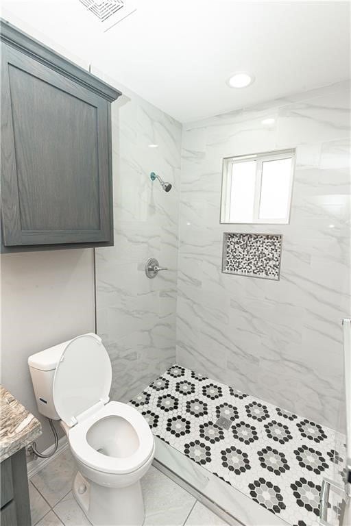 bathroom with toilet, a tile shower, and vanity