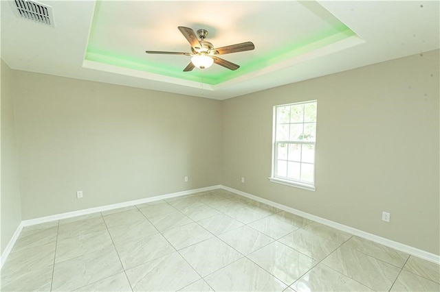 empty room with ceiling fan and a raised ceiling