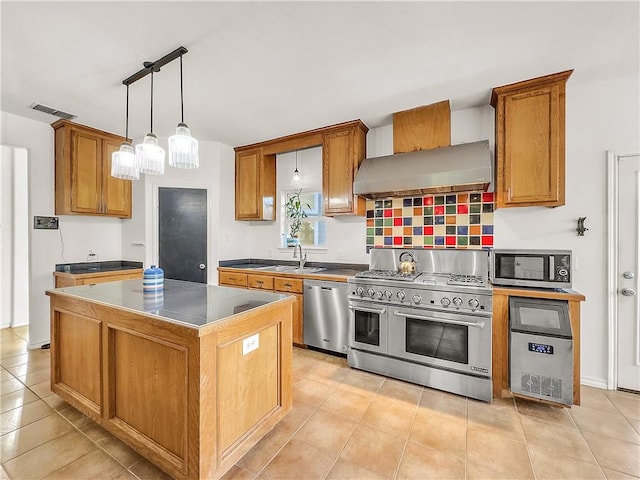 kitchen featuring sink, a center island, appliances with stainless steel finishes, pendant lighting, and wall chimney range hood