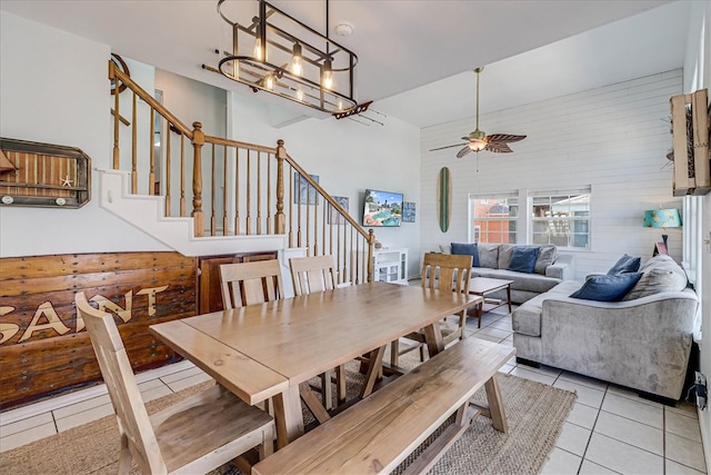 dining area with wood walls, a high ceiling, ceiling fan with notable chandelier, and light tile patterned floors