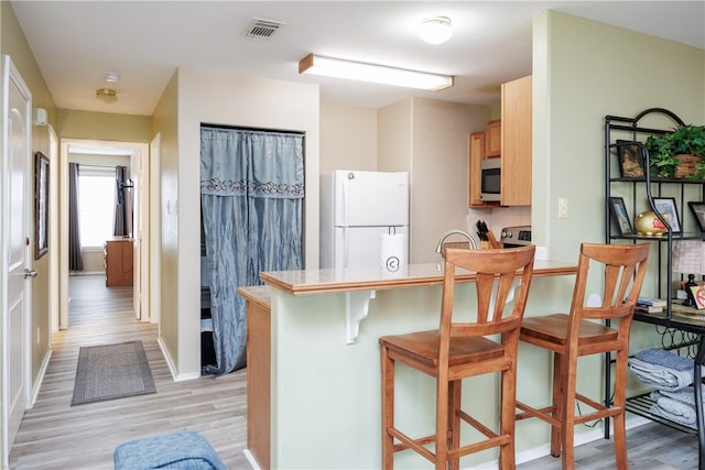 kitchen featuring kitchen peninsula, a kitchen breakfast bar, light brown cabinets, light hardwood / wood-style flooring, and white fridge