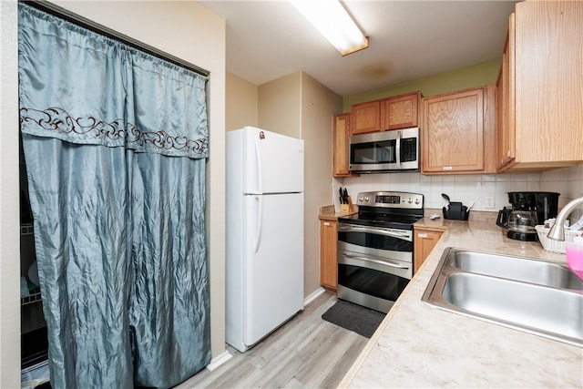 kitchen with tasteful backsplash, appliances with stainless steel finishes, light brown cabinetry, sink, and light hardwood / wood-style floors