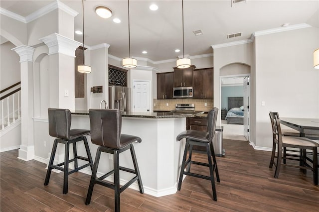 kitchen with a breakfast bar area, dark stone countertops, dark brown cabinets, stainless steel appliances, and decorative light fixtures