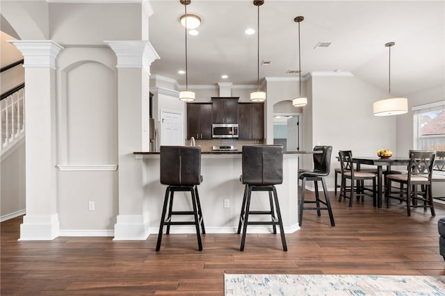 kitchen with a kitchen bar, dark brown cabinets, kitchen peninsula, pendant lighting, and stainless steel appliances