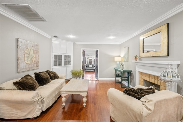 living room with ornamental molding, a tiled fireplace, wood-type flooring, and a textured ceiling