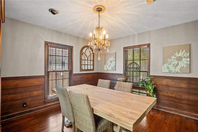 dining area featuring a textured ceiling, wood walls, dark hardwood / wood-style floors, and an inviting chandelier