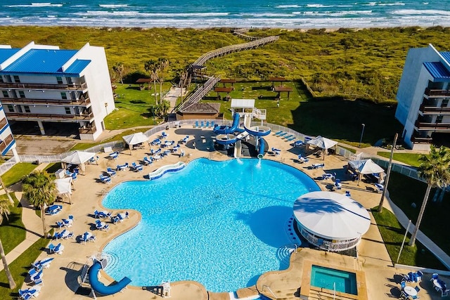 view of swimming pool with a water view, a water slide, and a view of the beach