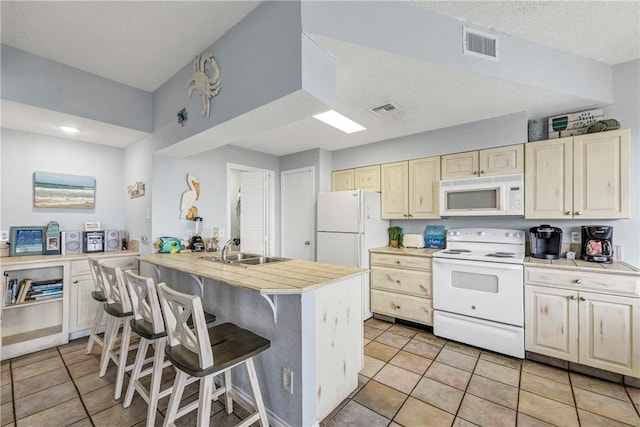 kitchen with light tile patterned flooring, sink, a breakfast bar area, and white appliances