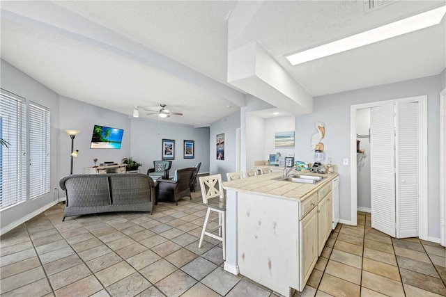 kitchen featuring a kitchen bar, sink, tile counters, kitchen peninsula, and ceiling fan