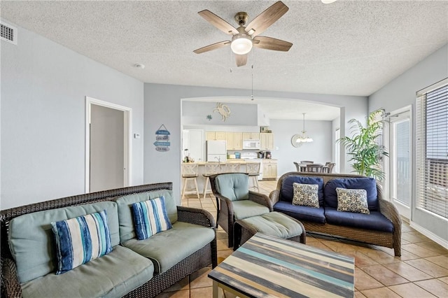 tiled living room with ceiling fan with notable chandelier and a textured ceiling