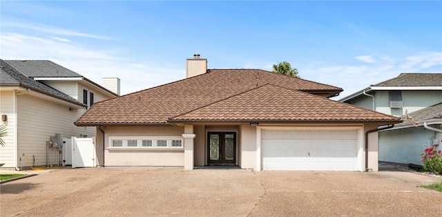 view of front facade featuring a garage, stucco siding, a chimney, french doors, and driveway