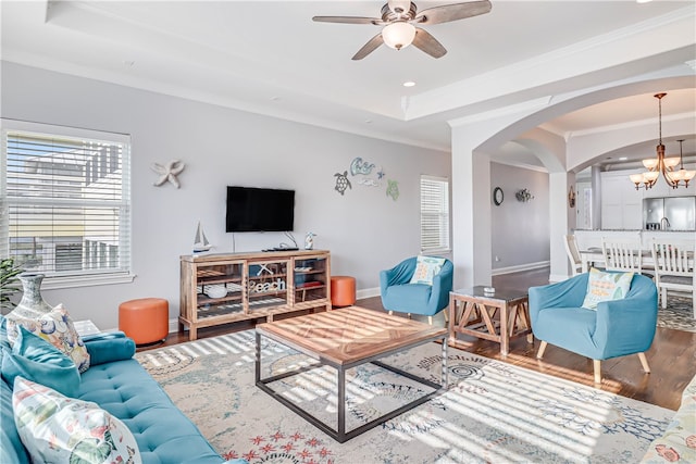 living room featuring wood-type flooring, a tray ceiling, ceiling fan with notable chandelier, and ornamental molding