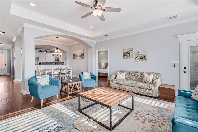 living room with ceiling fan with notable chandelier, a raised ceiling, dark hardwood / wood-style floors, and crown molding