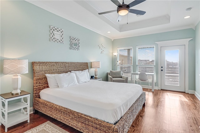 bedroom featuring ceiling fan, access to exterior, a tray ceiling, and wood-type flooring