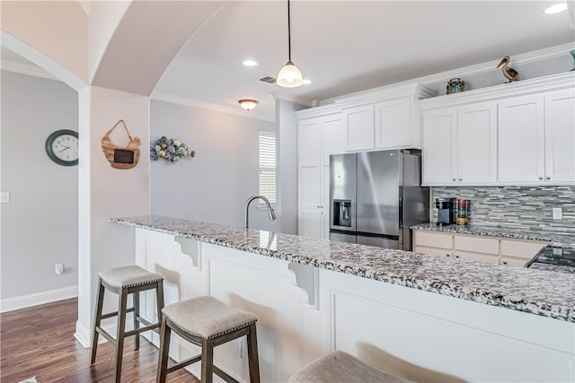 kitchen with stainless steel fridge, white cabinetry, light stone counters, and ornamental molding