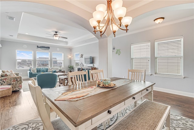 dining space featuring wood-type flooring, crown molding, ceiling fan with notable chandelier, and a tray ceiling