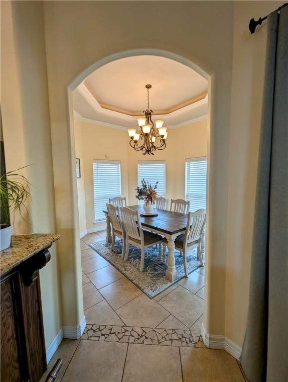 dining room featuring a healthy amount of sunlight, baseboards, a tray ceiling, and arched walkways