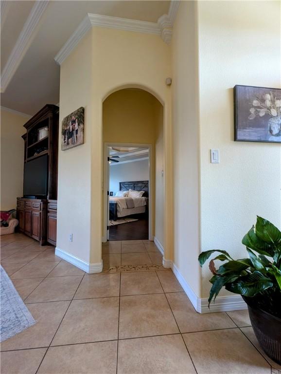 hall with arched walkways, ornamental molding, light tile patterned floors, and baseboards