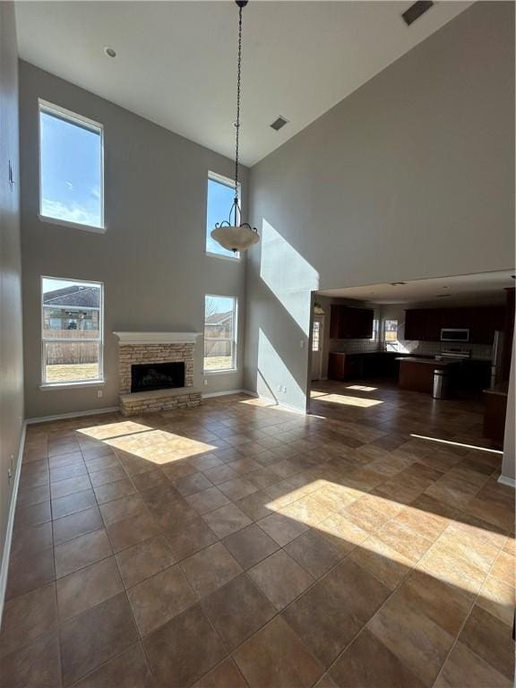 unfurnished living room featuring a stone fireplace, a towering ceiling, and dark tile patterned flooring