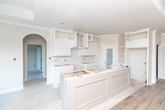 112 Shoalwater Way, Rockport, TX 78382 - kitchen with a center island, crown molding, arched walkways, white cabinetry, and light wood finished floors