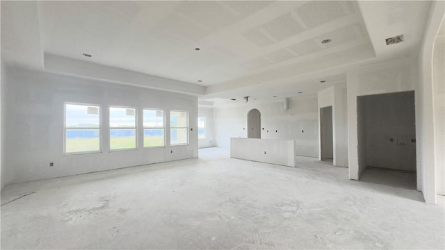 unfurnished living room featuring a raised ceiling, arched walkways, and visible vents