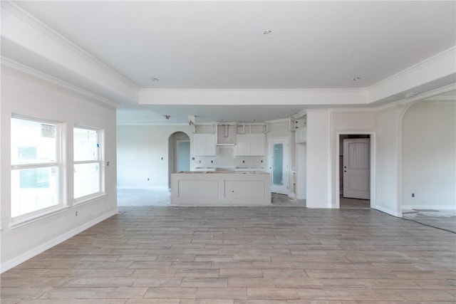 112 Shoalwater Way, Rockport, TX 78382 - unfurnished living room featuring arched walkways, a tray ceiling, crown molding, and light wood-type flooring